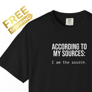 Puede incluir: Una camiseta negra de manga corta con texto blanco impreso en el pecho que dice: "ACCORDING TO MY SOURCES: I am the source." La prenda tiene un cuello redondo y un corte estándar, con una etiqueta de marca visible en el interior del cuello.