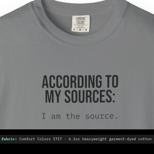 May include: A grey crew neck t-shirt featuring the black printed text ACCORDING TO MY SOURCES: I am the source. The shirt has a Comfort Colors brand label at the inner neckline indicating a size large and 6.1 ounce heavyweight cotton fabric.