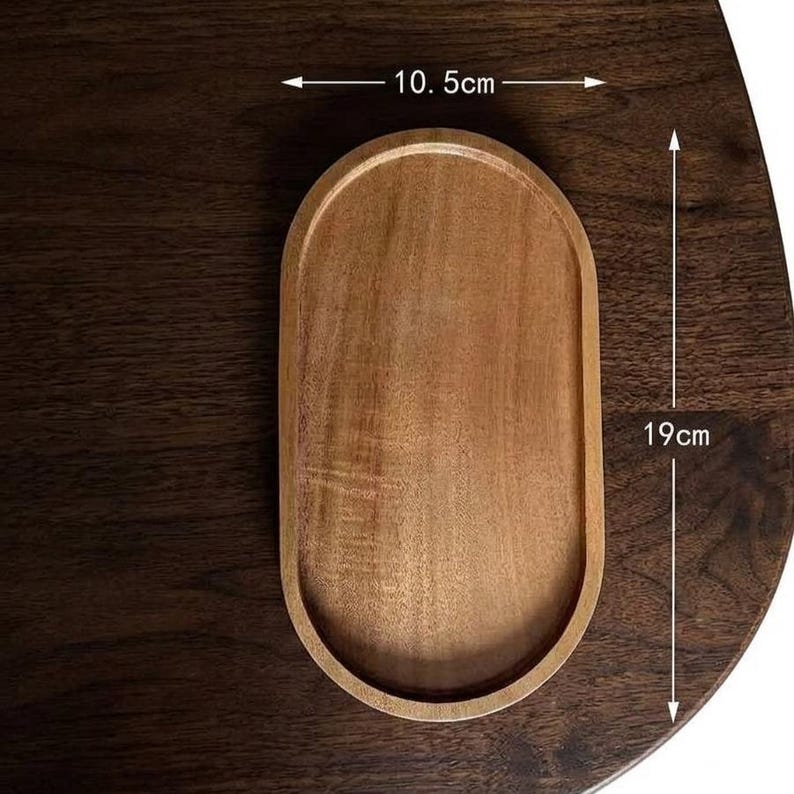 May include: An oval wooden tray with a smooth, light brown finish and a raised rim. The tray features clear measurement markings indicating a width of 10.5 cm and a length of 19 cm, which is approximately 4.13 inches by 7.48 inches in total size.