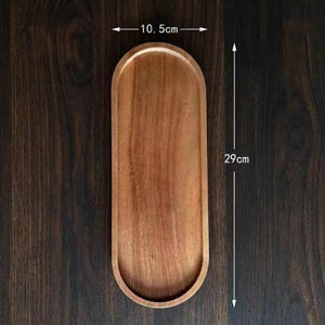 May include: An oval wooden tray with a smooth, light brown finish and visible wood grain. The tray features a width of 10.5 cm and a length of 29 cm, as indicated by the measurement text and arrows clearly printed on the image.