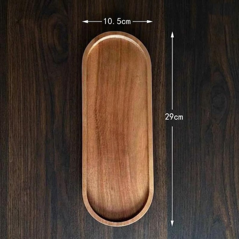 May include: An oval wooden tray with a smooth, light brown finish and visible wood grain. The tray features a width of 10.5 cm and a length of 29 cm, as indicated by the measurement text and arrows clearly printed on the image.