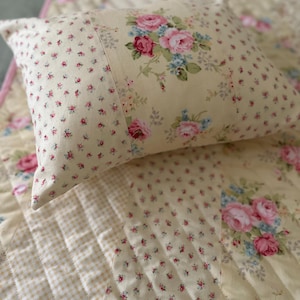 Peut inclure: Un ensemble de coussin et de courtepointe crème avec un motif de roses fleuries. L'oreiller présente un grand bouquet de roses roses et bleues, tandis que la courtepointe a un imprimé floral plus petit et un motif à carreaux. L'ensemble est matelassé.