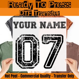 May include: A Ready To Press DTF Transfer sheet featuring the text YOUR NAME in a black varsity font above the large black distressed numbers 07. The design is displayed on a transparent film, intended for heat application onto various colored t-shirts.