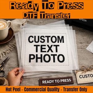 May include: A stack of DTF transfer sheets with the words "CUSTOM TEXT PHOTO" printed on them. The image also includes the text "Ready To Press" and "Hot Peel - Commercial Quality - Transfer Only". A cup of coffee and scissors are also visible.