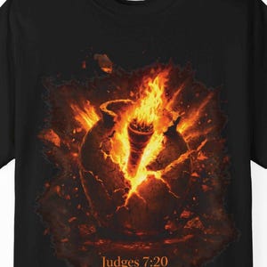May include: Black t-shirt featuring a fiery graphic design. The design depicts a cracked, glowing vessel with flames erupting from within. The text "Judges 7:20" is printed below the image. The shirt is made by Comfort Colors.
