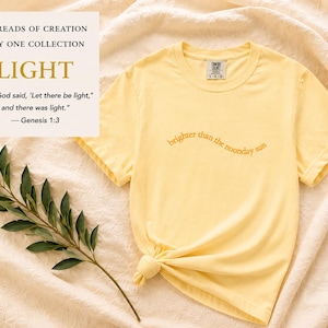 Op de afbeelding: Een lichtgeel t-shirt met de tekst "brighter than the noonday sun" in een gebogen lettertype. Het shirt heeft ook een kleine geborduurde "1" op de mouw. De afbeelding bevat de tekst "THREADS OF CREATION DAY ONE COLLECTION LIGHT".
