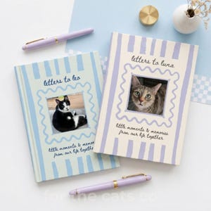 May include: Two cat-themed journals with photos of cats inside, titled "Letters to Leo" and "Letters to Luna." The journals have a light blue and white striped design with matching pens. The phrase "little moments & memories from our life together" is also on the journals.