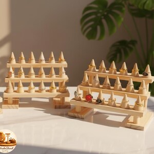May include: Wooden ring display stands with multiple tiers. Each tier features small, cone-shaped holders for rings. The stands are made of light-colored wood and are designed to showcase jewelry. The stands are on a white surface.