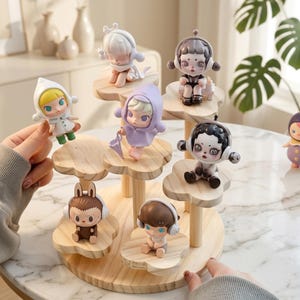 May include: A multi-tiered wooden display stand with a light wood grain finish and cloud-shaped platforms. Seven small, stylized vinyl figurines with various hair colors, outfits, and headphones are arranged on the different levels of the stand.