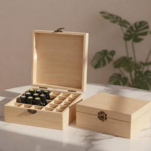 May include: A light-colored wooden essential oil storage box, open to reveal small bottles. The box has a hinged lid and a brass-colored clasp. The box is sitting on a white surface.