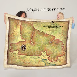 May include: A tan and brown throw blanket with a vintage map of The Absaroka-Beartooth Wilderness in Montana. The map shows the location of mountains, rivers, and other landmarks. The blanket is made of soft, comfortable fleece and is perfect for snuggling up on the couch.