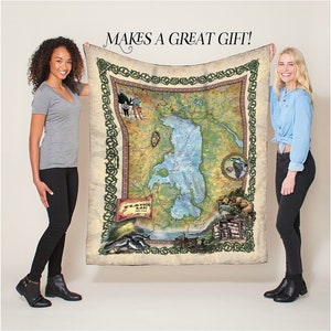 May include: A soft, plush fleece blanket featuring a detailed map of Flathead Lake, Montana. The map is surrounded by a decorative green border and includes various illustrations of local wildlife and activities. The text "Flathead Lake" is prominently displayed on the map.
