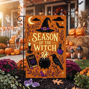 Op de afbeelding: Een rechthoekige oranje tuin vlag met de tekst Season of the Witch in crèmekleurige letters. Het ontwerp bevat een zwarte heksenhoed, een brandende kaars, een paarse toverdrankfles, een spreukenboek met de tekst Magic, een ketel en een zwarte kraai.