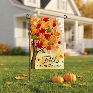 May include: A rectangular garden flag featuring a tree with vibrant red, orange, yellow, and green autumn leaves. The text "FALL is in the air" is printed in black cursive script against a soft yellow background on the lower portion.
