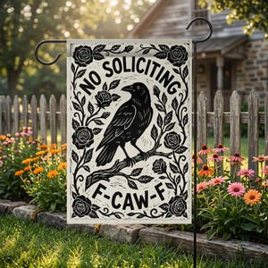 Op de afbeelding: Een tuinvaandel met een zwart-wit ontwerp. De vlag toont een raaf op een tak, omringd door rozen en de tekst "NO SOLICITING" en "F-CAW-F". De vlag wordt in een tuin getoond.
