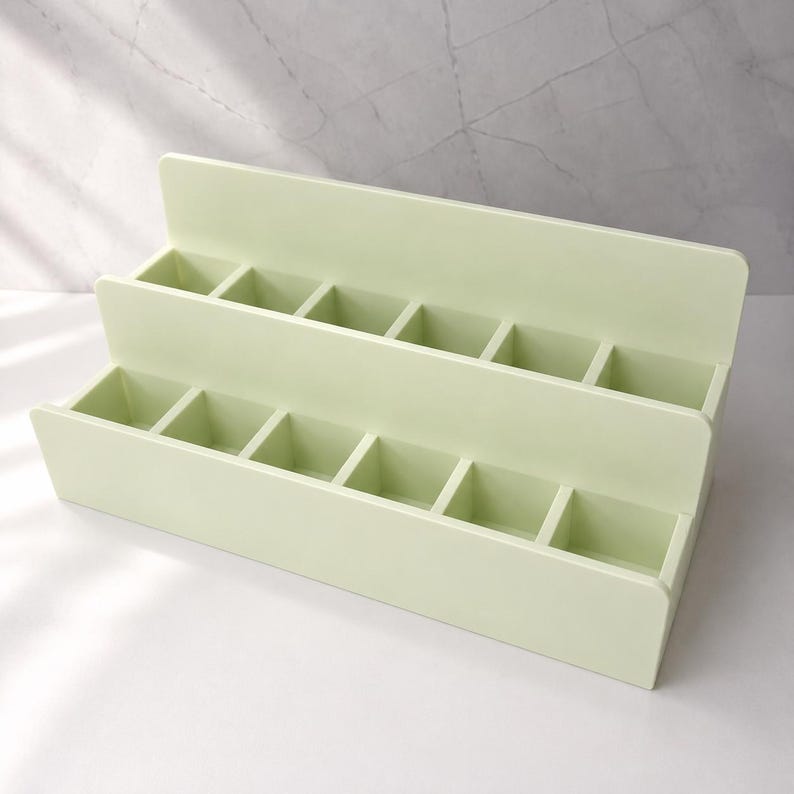 Puede incluir: Un organizador escalonado de color verde claro con dos niveles y seis compartimentos cuadrados en cada fila. La estructura est&aacute; hecha de un material s&oacute;lido y liso con acabado mate, dise&ntilde;ado con una disposici&oacute;n en niveles para organizar.