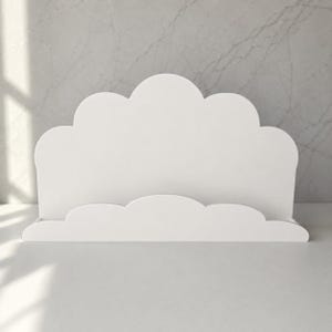 May include: A white cloud-shaped display stand featuring a smooth, matte finish. The structure consists of a tall, scalloped back panel and a shorter, matching scalloped front ledge, creating a slot for holding items in an upright position.
