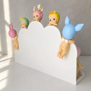 May include: A white cloud-shaped display stand featuring five small figurines with various animal-themed headgear, including a pink rabbit, green bird, floral deer, yellow duck, and blue rabbit, all perched along the top edge of the stand.