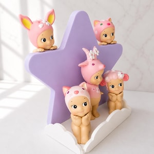 Op de afbeelding: Een verzameling kleine, grillige beeldjes, elk versierd met een unieke hoed met dierenthema. De beeldjes staan in verschillende poses, met een zacht, pastelkleurig kleurenpalet. Ze zijn gerangschikt rond een grote, paarse stervormige display.