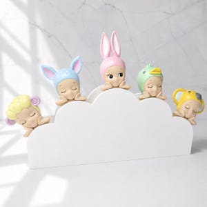 Peut inclure: Cinq figurines repr&eacute;sentant de petits personnages endormis, coiff&eacute;s de chapeaux d'animaux diff&eacute;rents, pos&eacute;s sur une &eacute;tag&egrave;re blanche en forme de nuage. Les chapeaux sont en forme de mouton, de lapin, de canard et de koala, aux couleurs pastel.