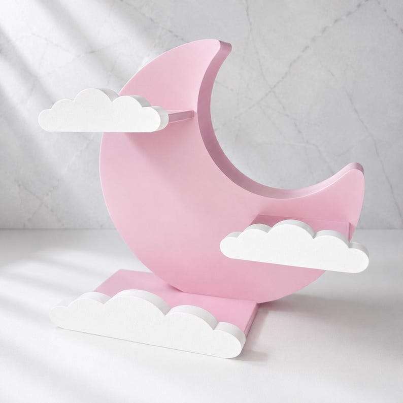 May include: A pink, crescent moon-shaped shelf with two white cloud shelves and a cloud-shaped base. The shelf is designed for decorative items and has a whimsical, dreamy aesthetic.