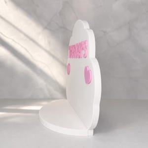 May include: A white cloud-shaped shelf featuring the pink text "TRACY'S" in raised lettering. The shelf includes two small pink heart-shaped accents positioned below the text on the front face of the cloud structure, which has a flat base.
