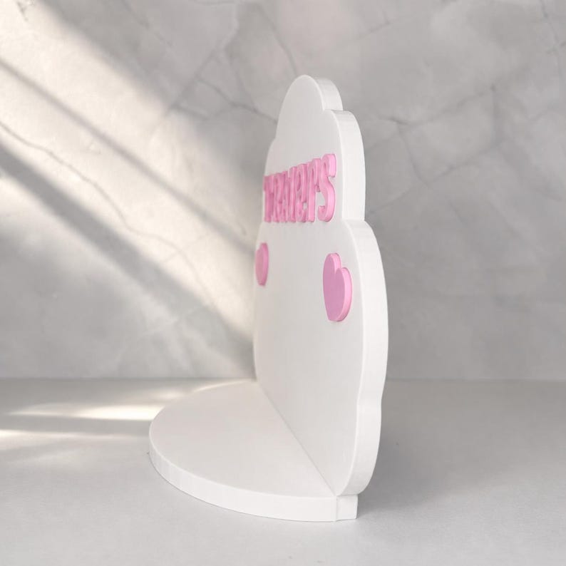 May include: A white cloud-shaped shelf featuring the pink text "TRACY'S" in raised lettering. The shelf includes two small pink heart-shaped accents positioned below the text on the front face of the cloud structure, which has a flat base.