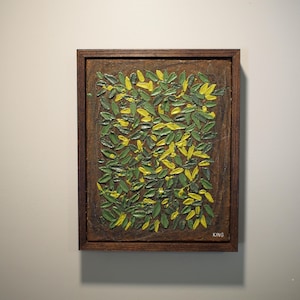 May include: A framed abstract painting featuring a textured surface with green and yellow leaf-like shapes. The artwork is encased in a dark brown wooden frame, creating a contrast with the lighter wall.