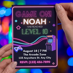 May include: A black invitation card with a neon pink border. The text "GAME ON!" and "NOAH HAS REACHED LEVEL 10" are displayed in white and green. The card includes a game controller and arcade machine graphic.