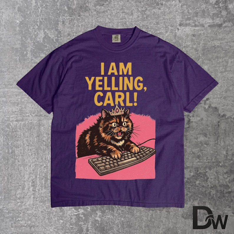 Pode incluir: Camiseta roxa com o texto "I AM YELLING, CARL!". O gr&aacute;fico apresenta um gato usando uma coroa, digitando em um teclado, em um fundo rosa. O gato &eacute; marrom e preto.