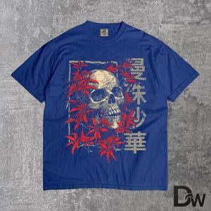 May include: A blue t-shirt with a skull graphic encircled by red leaves. The skull has visible teeth and eye sockets. Japanese characters are printed on the right side of the skull. The shirt has a crew neck and short sleeves.