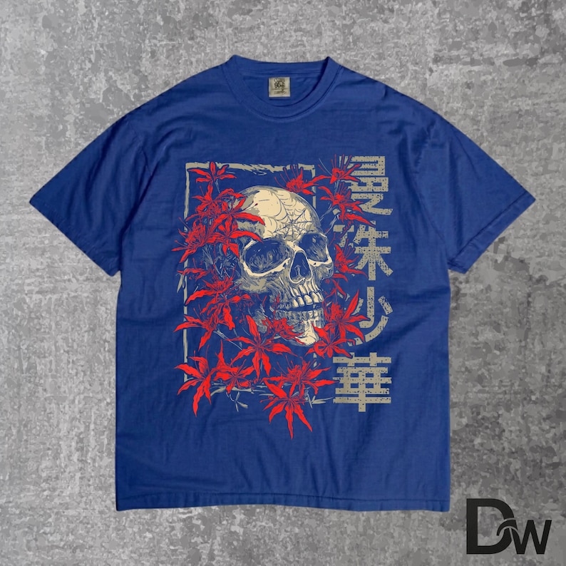 May include: A blue t-shirt with a skull graphic encircled by red leaves. The skull has visible teeth and eye sockets. Japanese characters are printed on the right side of the skull. The shirt has a crew neck and short sleeves.