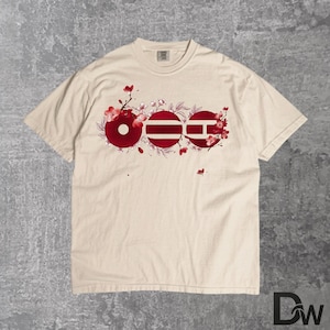 May include: Cream-colored t-shirt featuring a red floral design with the letters OEE. The design incorporates a circle, a striped circle, and a square with a horizontal line. The shirt has a crew neck and short sleeves.