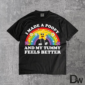 Könnte beinhalten: Schwarzes T-Shirt mit einem Regenbogen und einem Cartoon-Stern-Charakter. Der Text auf dem Shirt lautet: "I MADE A POOPY AND MY TUMMY FEELS BETTER". Das Design beinhaltet Blumen und einen lächelnden Stern.