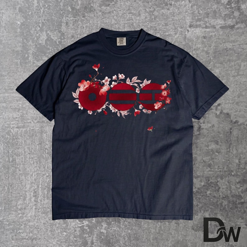 May include: Navy blue t-shirt with a floral design. The design features three red circles with horizontal stripes, surrounded by white flowers and red blossoms. The shirt is made of a soft material.