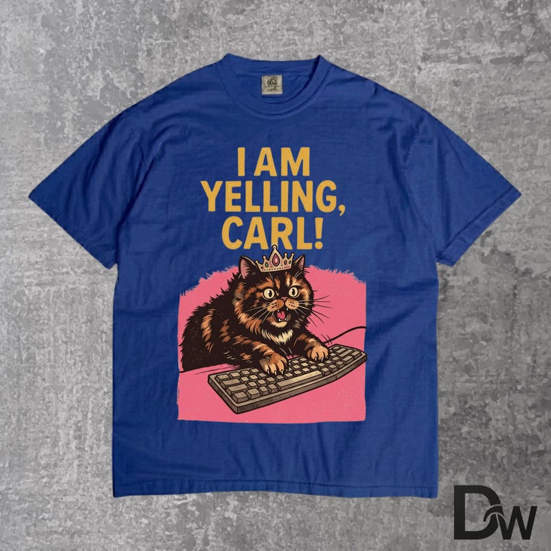 Pode incluir: Camiseta azul royal com um gato de desenho animado usando uma coroa e digitando em um teclado. O texto "I AM YELLING, CARL!" est&aacute; impresso acima do gato. O gato &eacute; marrom e preto com um fundo rosa.