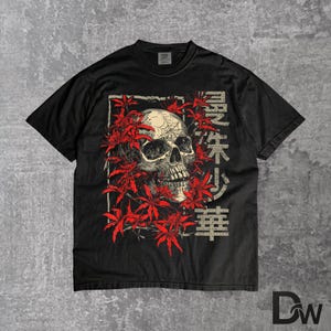 May include: Black t-shirt with a skull graphic framed by red flowers. Japanese characters are printed on the right. The tee has a crew neck and short sleeves, ideal for everyday wear. The design has a vintage aesthetic.