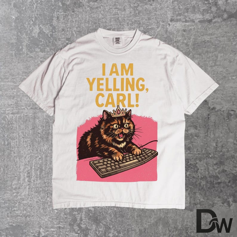 Pode incluir: Camiseta branca com o texto "I AM YELLING, CARL!". O gr&aacute;fico apresenta um gato com coroa, digitando em um teclado, sobre um fundo rosa. A camiseta tem gola redonda e mangas curtas.