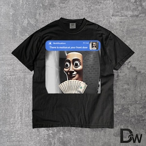 May include: A black t-shirt featuring a graphic print of a smartphone notification that reads, "Notification 6m ago There is motion at your front door." The graphic shows a stylised face holding a fan of US dollar bills in a doorway.