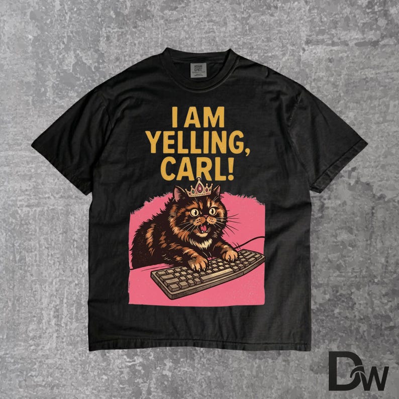 Pode incluir: Camiseta preta com um gato de desenho animado usando uma coroa e digitando em um teclado. O texto "I AM YELLING, CARL!" est&aacute; impresso acima do gato. O gato &eacute; marrom e preto com um fundo rosa.