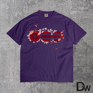 May include: A purple t-shirt featuring a floral design with the word "OOO" in red and white. The design incorporates cherry blossoms and a striped pattern within the letters. The shirt is made of a soft material.