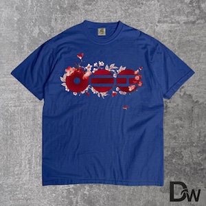 May include: A blue t-shirt featuring a red and white floral design with the letters "OGG" in red. The shirt is made of a soft material and has a crew neck. The design is centered on the front of the shirt.