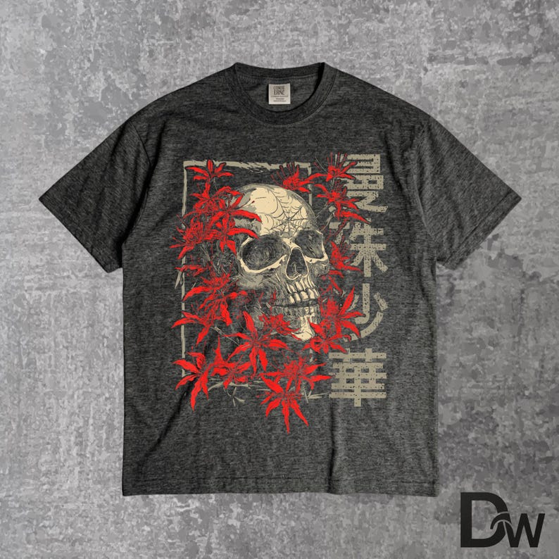 May include: Dark grey t-shirt with a skull graphic encircled by red leaves. Japanese characters are printed vertically on the right. The tee has a crew neck and short sleeves.