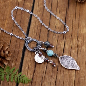 May include: A silver chain necklace with a silver charm featuring a circle, a leaf, and several beads. The beads are turquoise, brown, and black.
