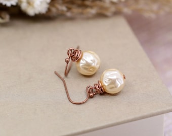 May include: A pair of pearl earrings with copper wire wrapping. The pearls are a cream color and the wire is a rose gold color.