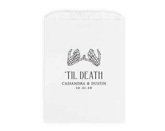May include: White paper favor bag with a black skeleton hand design and the text 'Til Death, Cassandra & Dustin 10.31.26'.