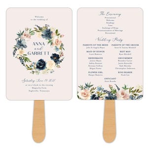 May include: Two-sided wedding fan with a wooden handle. The front features the names "Anna and Garrett" within a floral wreath. The back lists the ceremony details and wedding party. The design includes navy, blush, and cream colors.