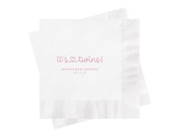 May include: Two stacked white paper napkins featuring light pink text that reads it's twins! with a heart icon, followed by the text JENNA'S BABY SHOWER and the date 10.15.27 printed in a simple sans-serif font centered on the top napkin.