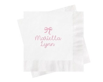 May include: Two square white paper napkins stacked on top of each other. The top napkin features a light pink graphic of a bow centered above the text Mariella Lynn printed in a matching light pink cursive script font on the center surface.