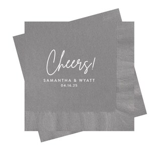 May include: Two square gray paper napkins stacked at an angle. The top napkin features the white printed text Cheers! in a script font, followed by the names SAMANTHA & WYATT and the date 04.16.25 in a clean, sans-serif capital typeface.